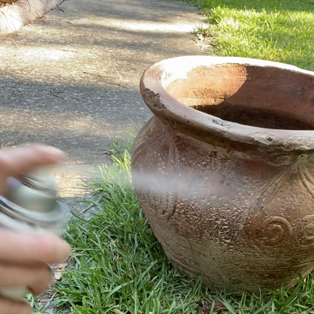 hand spraying sealer on a terra cotta pot
