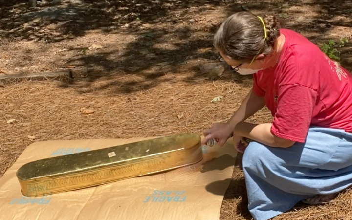 woman spray painting a long brass container