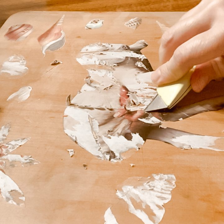 woman scraping stickers off of cutting board with x-acto knife