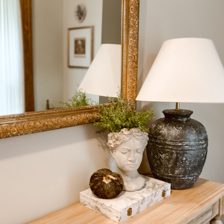 marble box displayed on a console table with a head planter, pumpkin and lamp