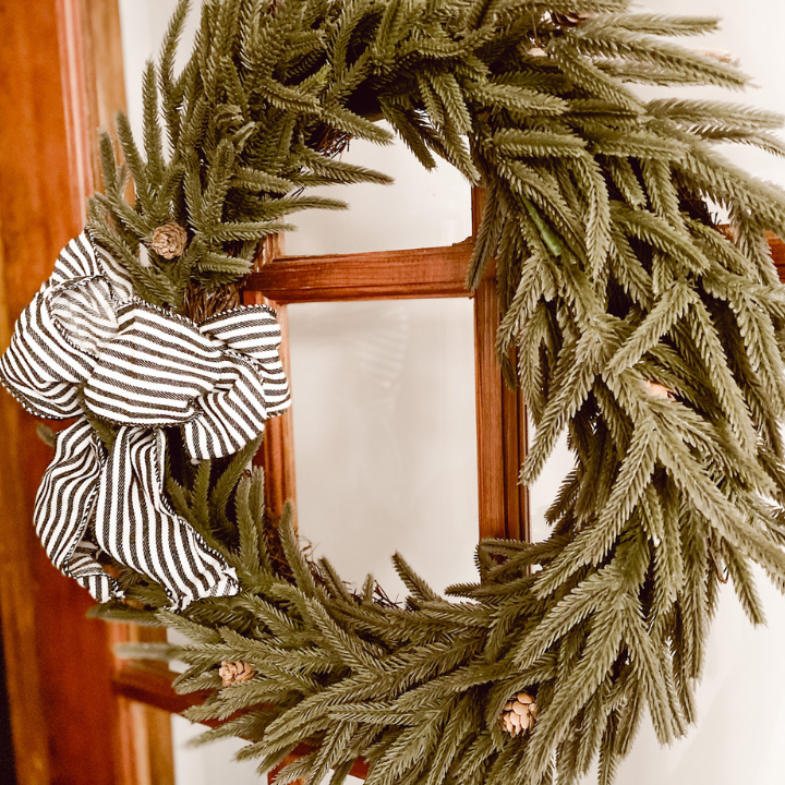 green Christmas wreath with a black and white bow hanging on a door