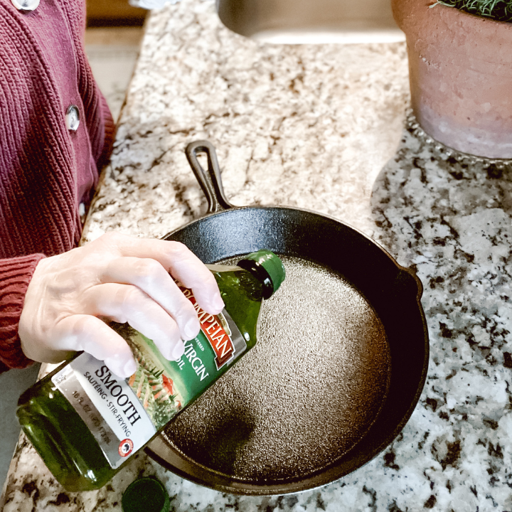 woman putting oil into a cast iron skillet to season it