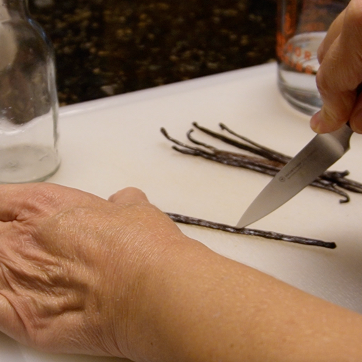 woman cutting vanilla beans down the middle to make homemade vanilla extract