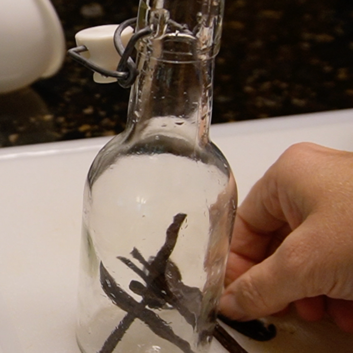 woman adding vanilla beans to a bottle for making homemade vanilla beans